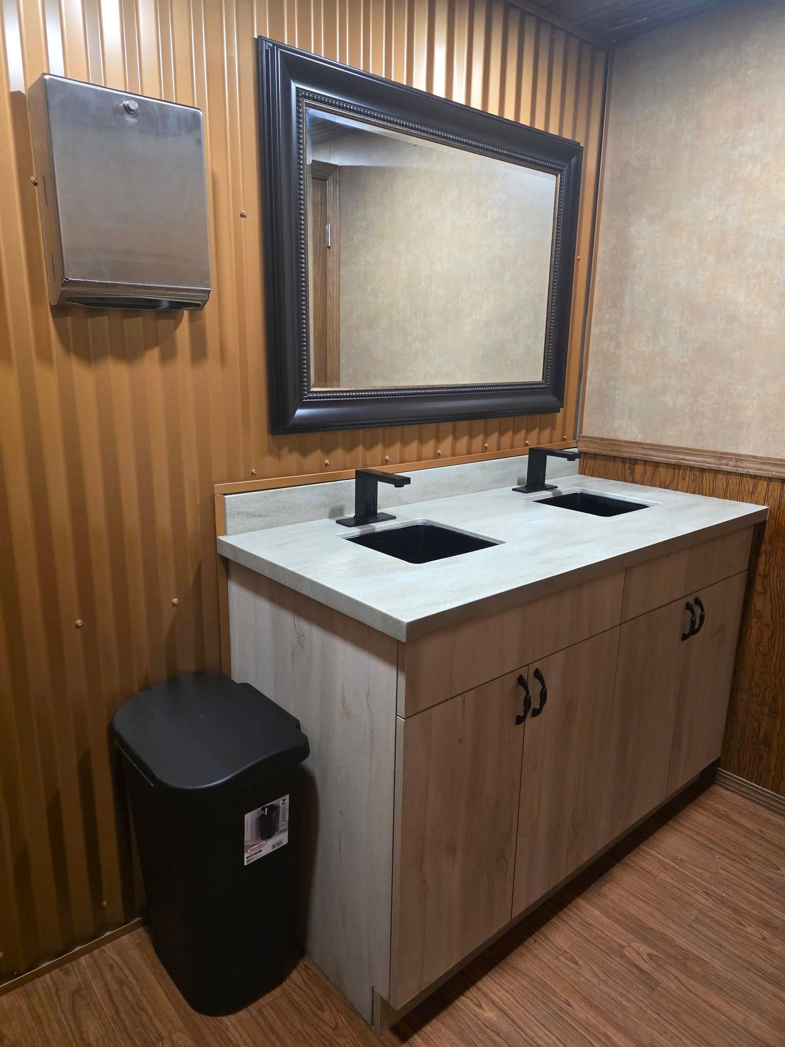 A dual-sink vanity with matte black faucets and a large ornate framed mirror against a corrugated metal wall.
