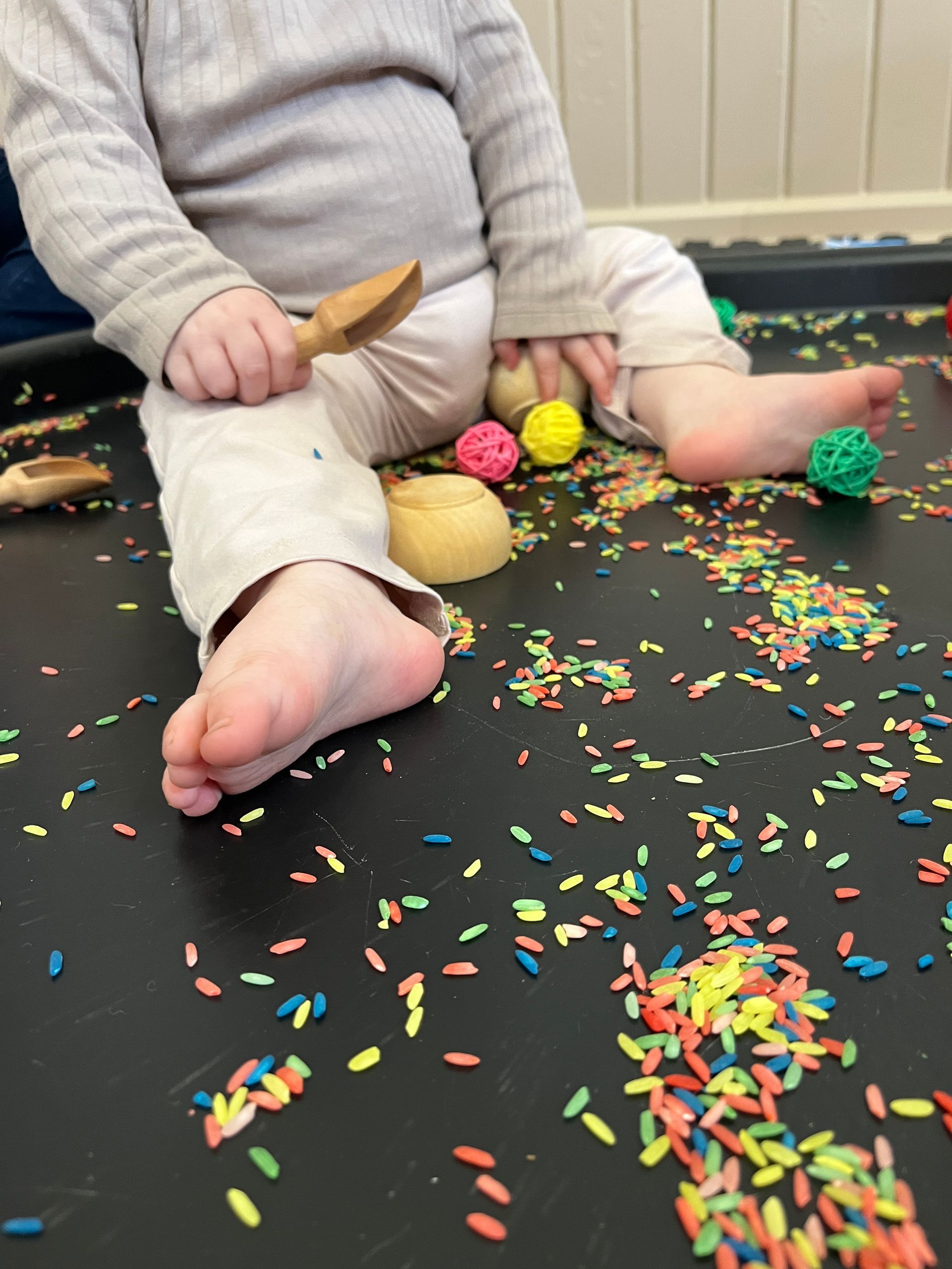 a child playing in a  tuff tray of rainbow rice