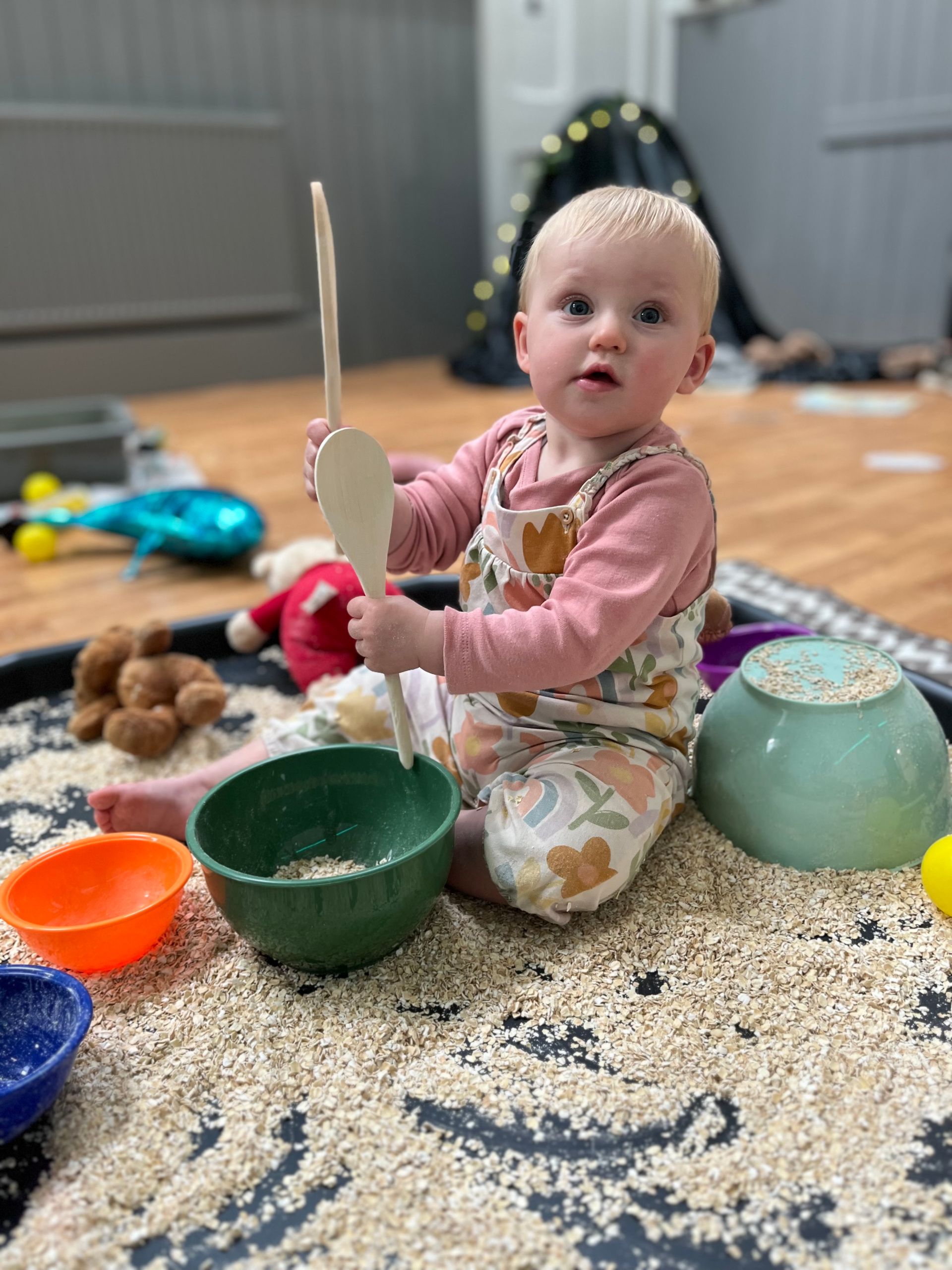 a child playing with wooden spoons and dry oats