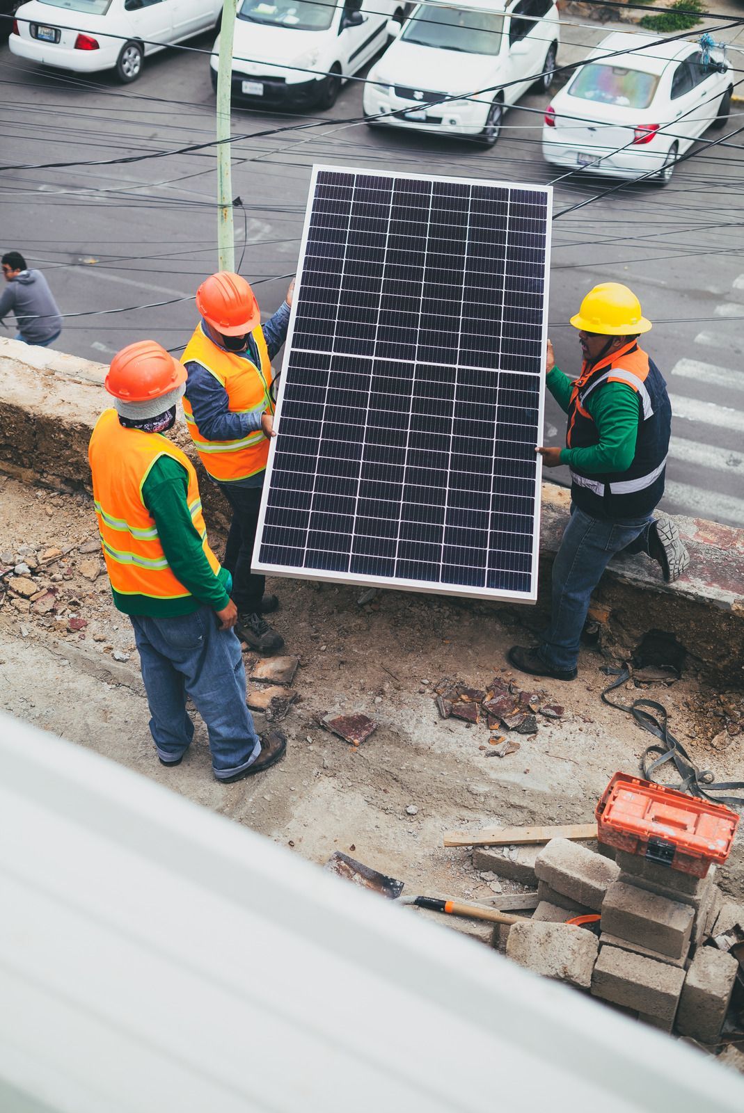 Workers in orange vests and hard hats carrying a solar panel at a construction site