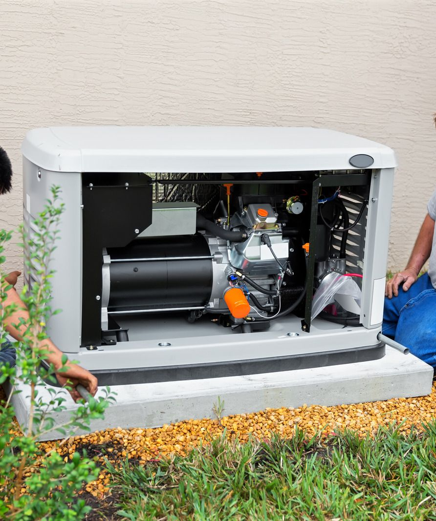 Open generator inside a white enclosure beside a house, with grass and leaves in front.