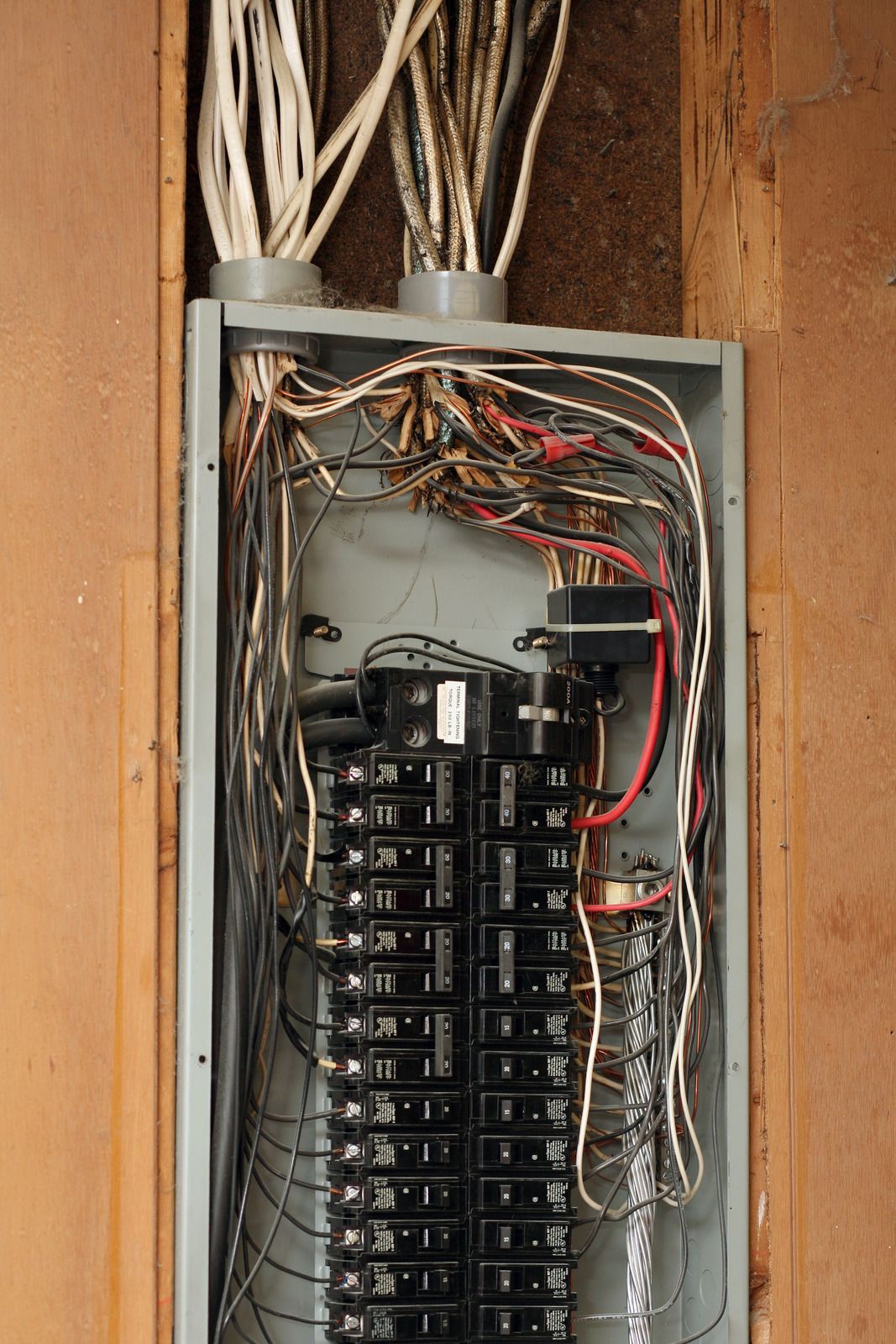 Open electrical breaker panel with door ajar in a wooden wall.
