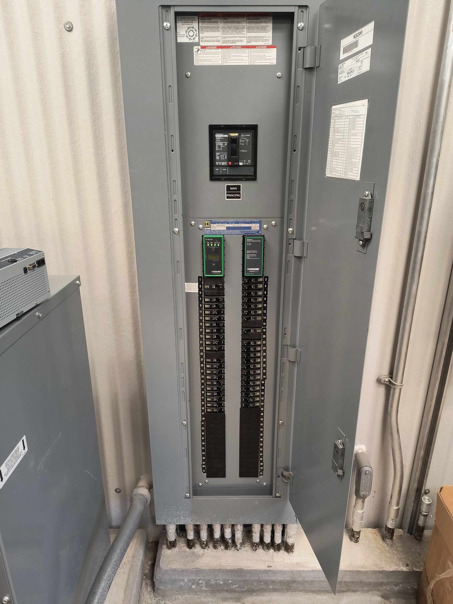 Open electrical breaker panel in a utility room with a door ajar.
