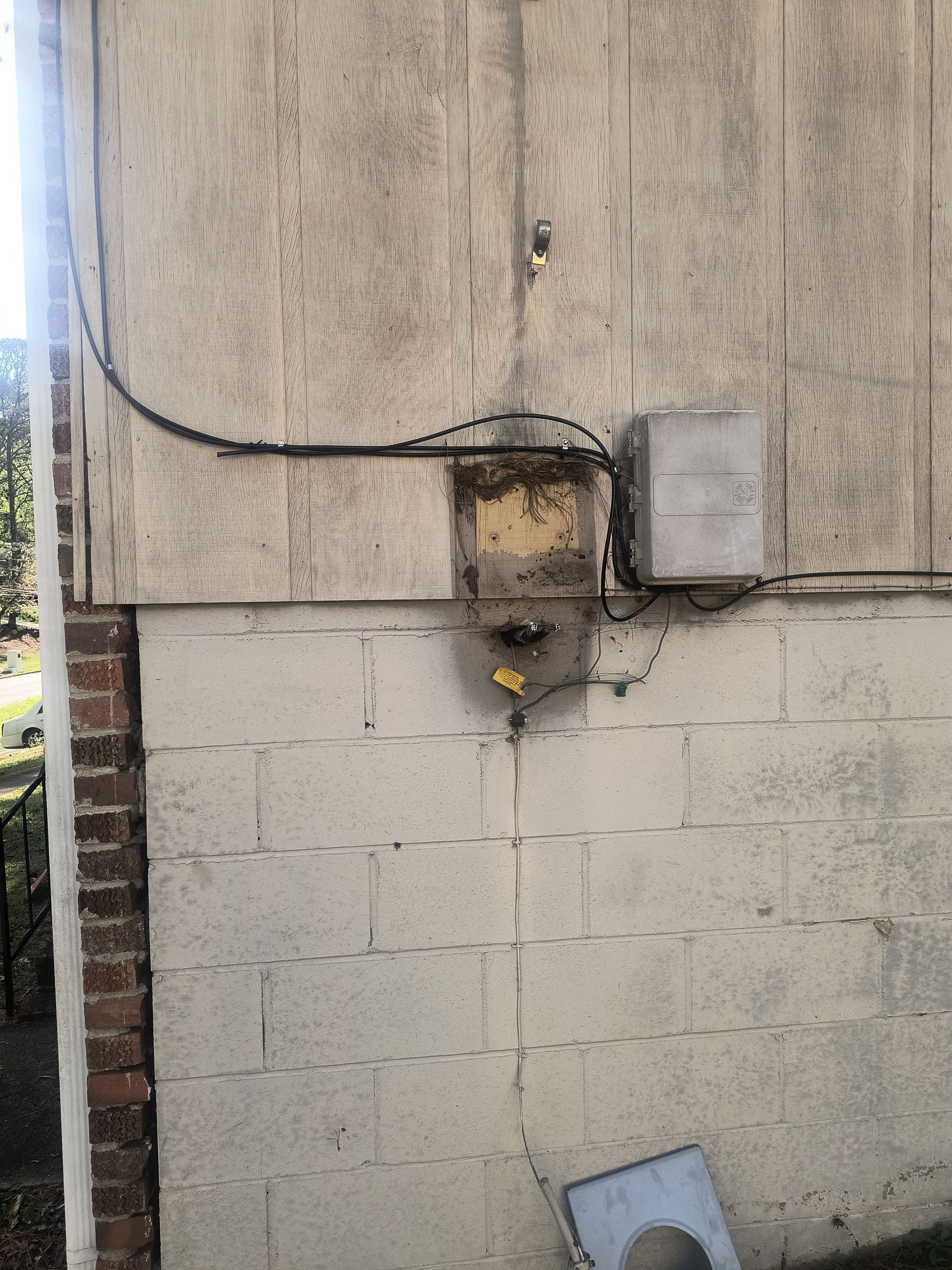 Damaged utility meter on a wall with exposed wiring and a hanging metal panel