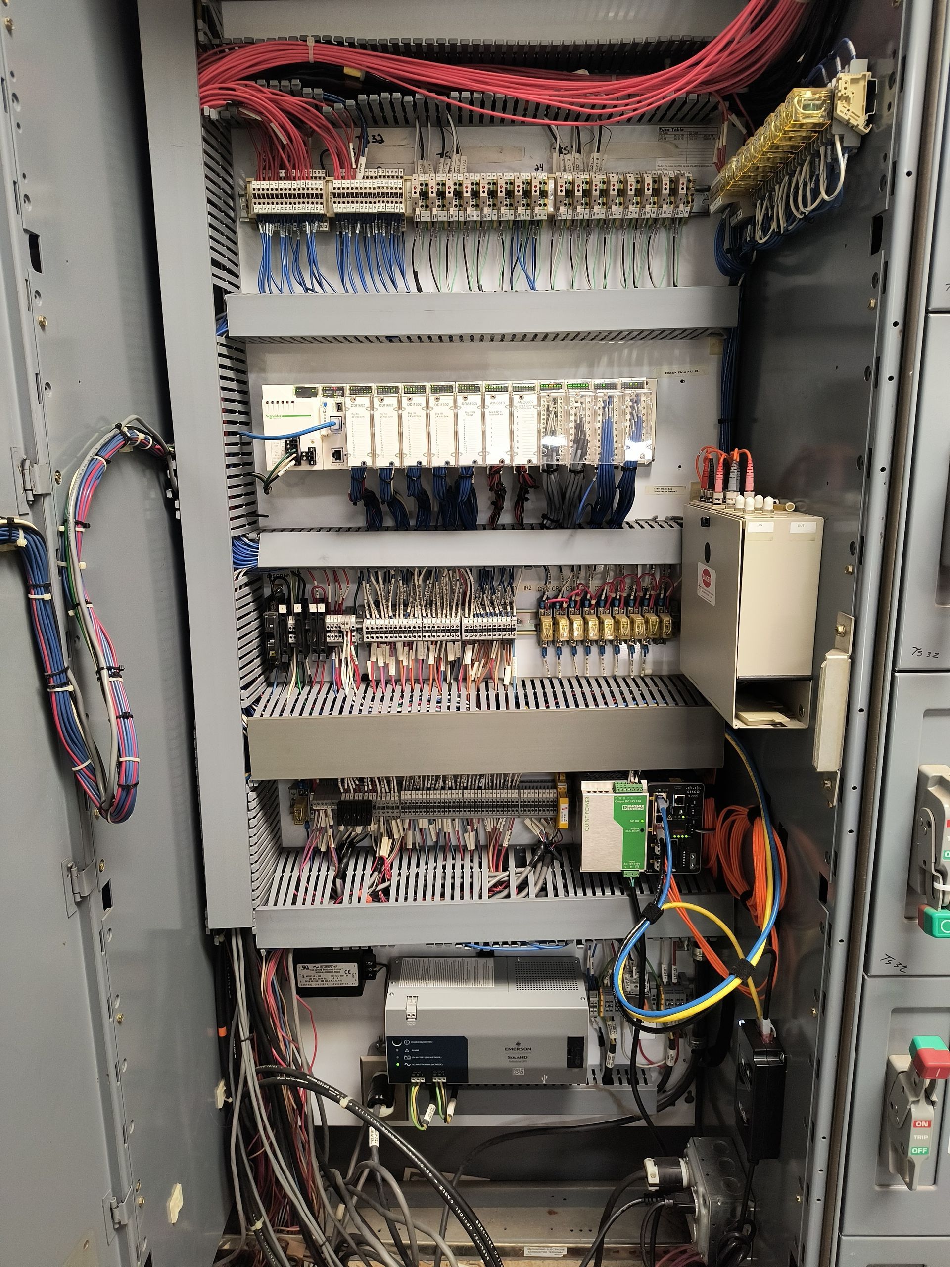 Open electrical control panel with wiring, relays, and circuit modules inside a gray cabinet