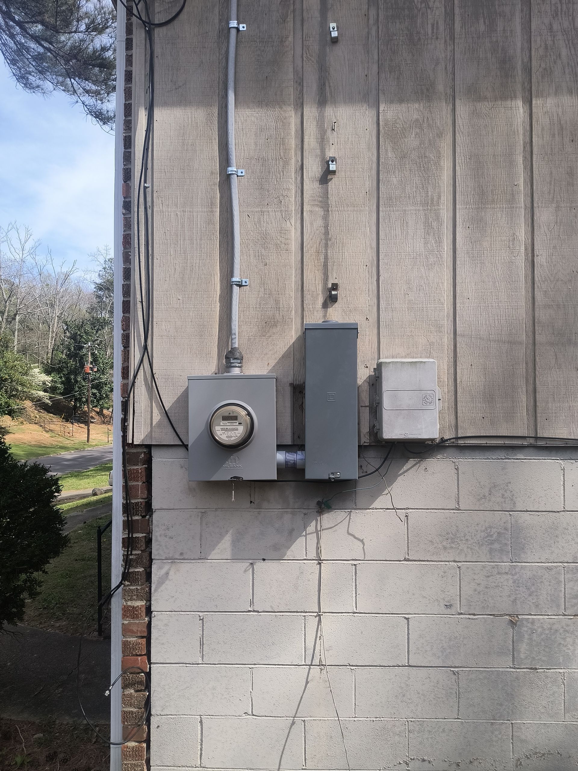 Exterior wall with electrical meter, conduit, and utility boxes on gray concrete block wall