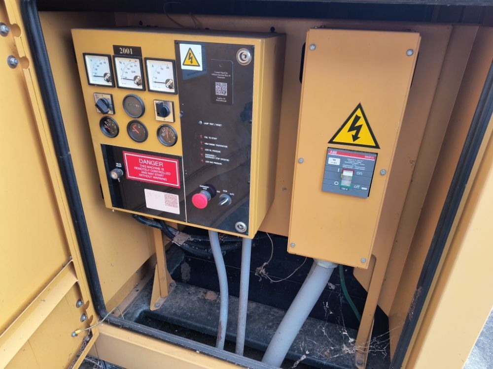 Yellow industrial control panel with gauges, switches, warning signs, and red emergency stop button inside equipment cabinet