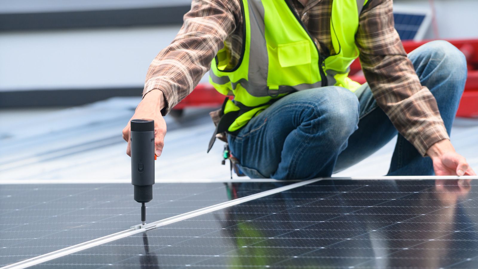 Worker in a neon safety vest installs solar panels with a power drill.