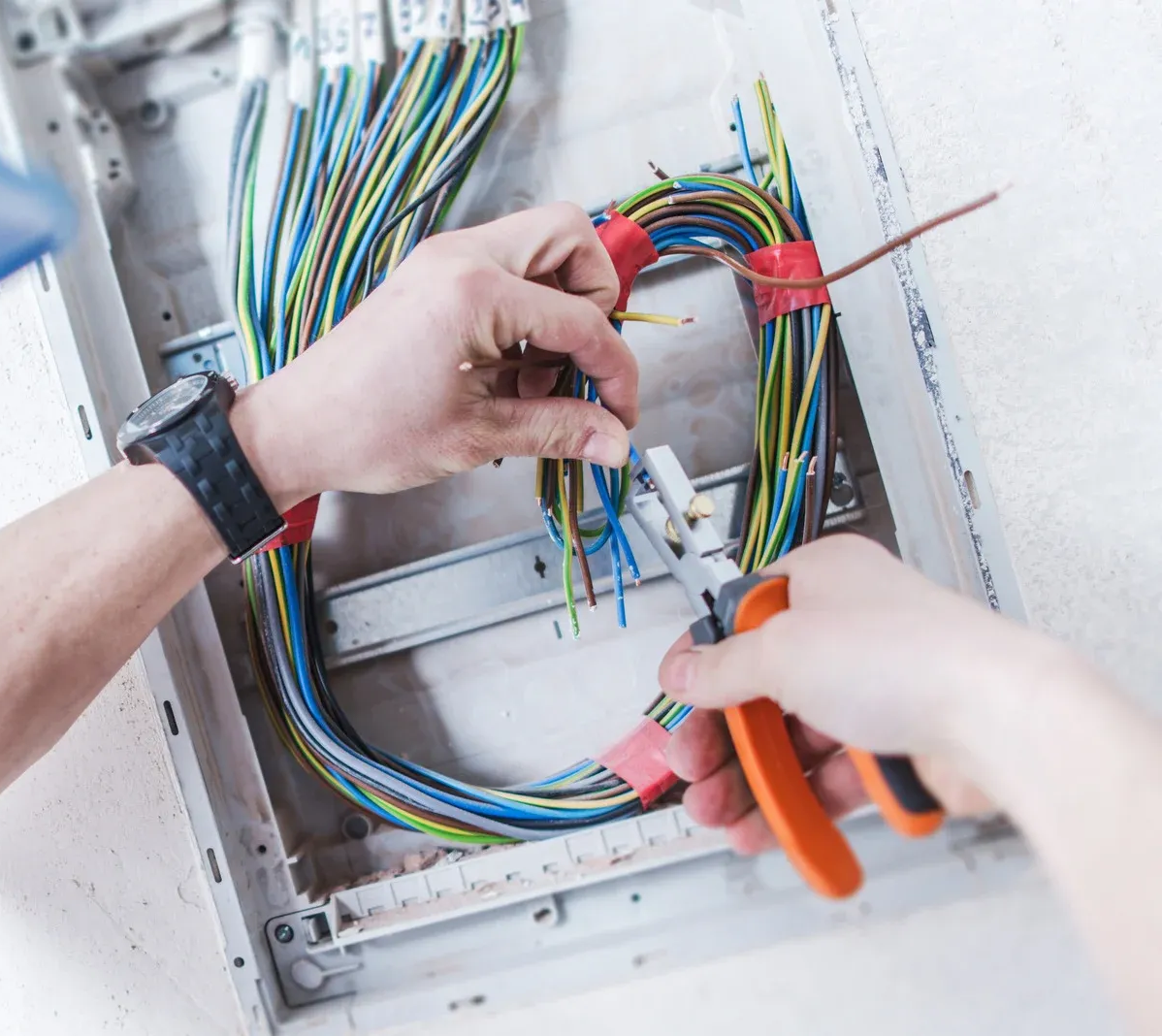 Hands wiring a circuit box with multicolored cables and orange pliers