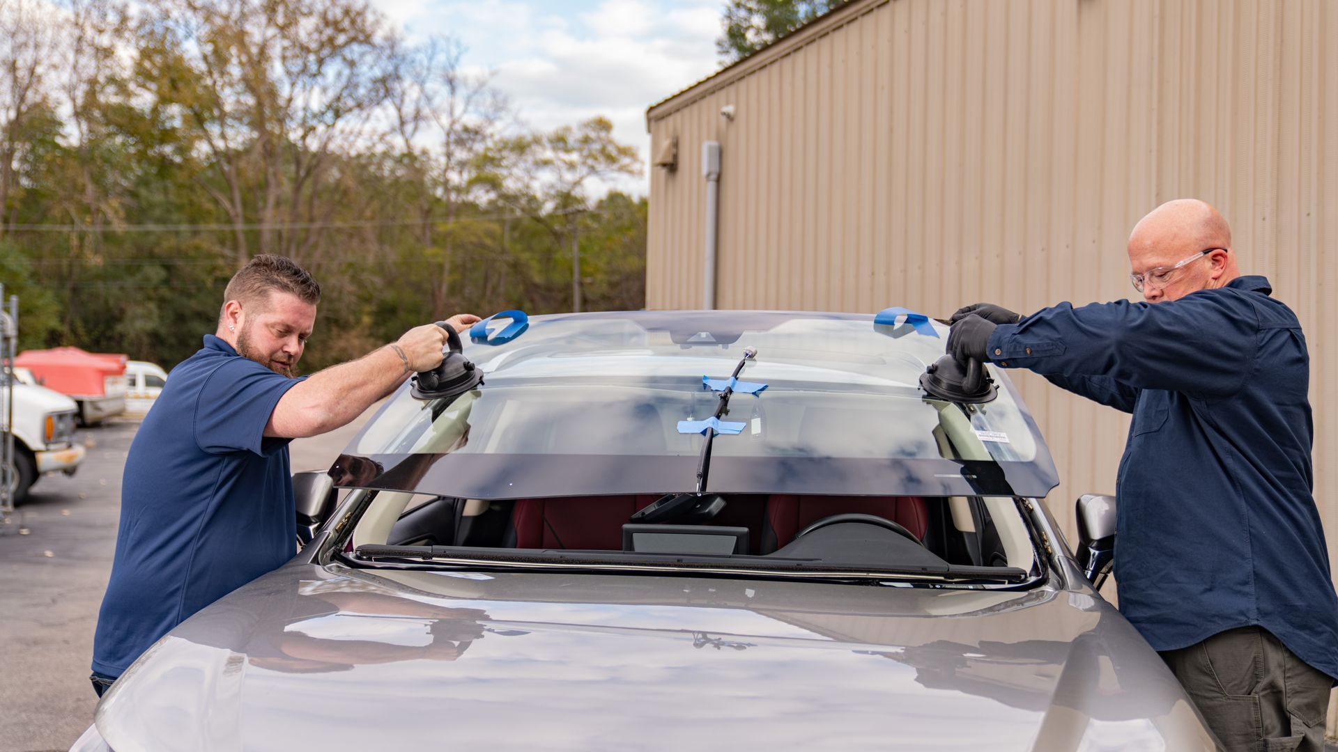 Gloved hands using a red suction tool to repair a car windshield
