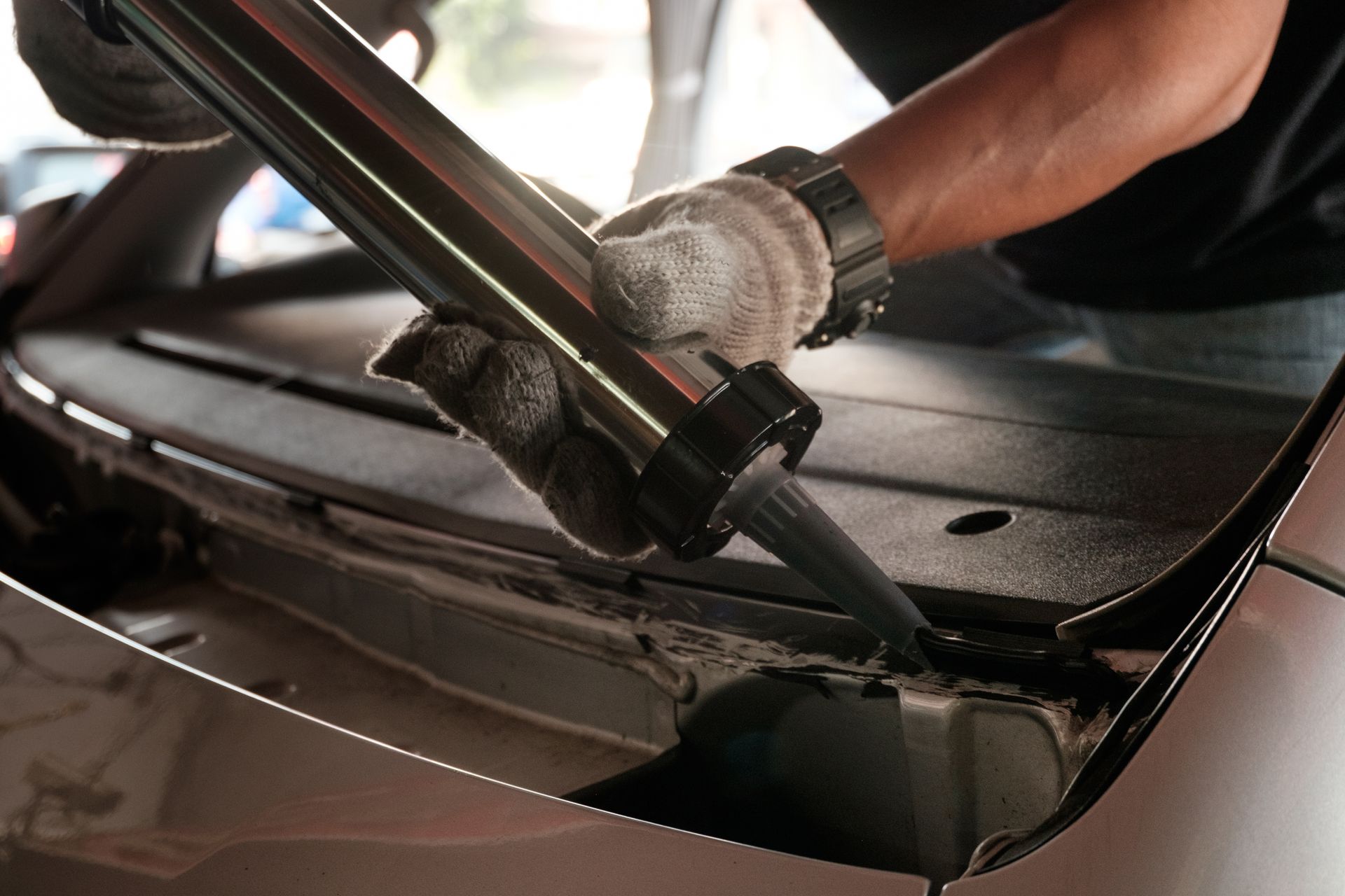 Gloved hands using a windshield wiper tool on a car windshield in close-up