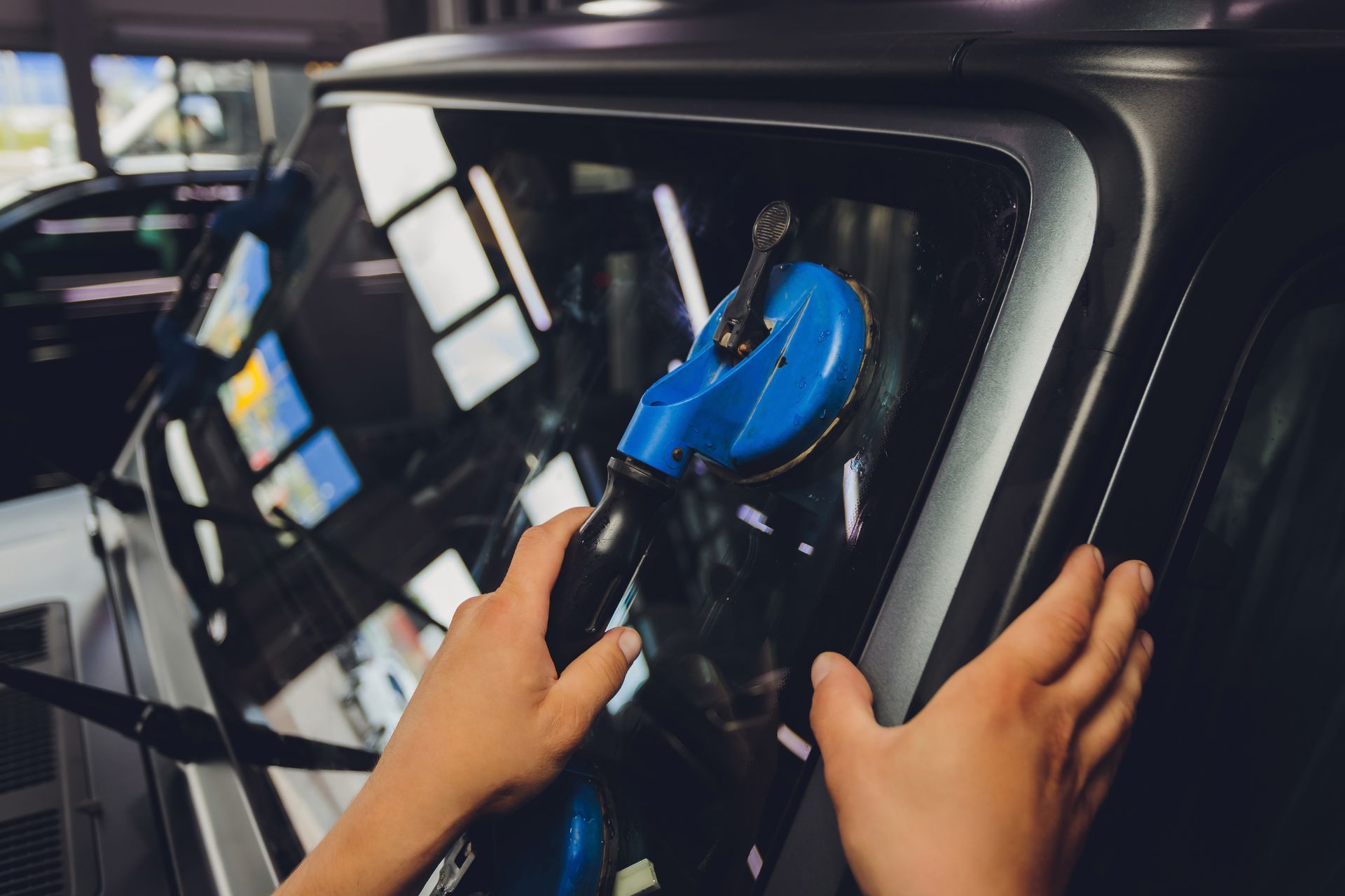 Hands securing a blue vacuum attachment inside a car window during cleaning