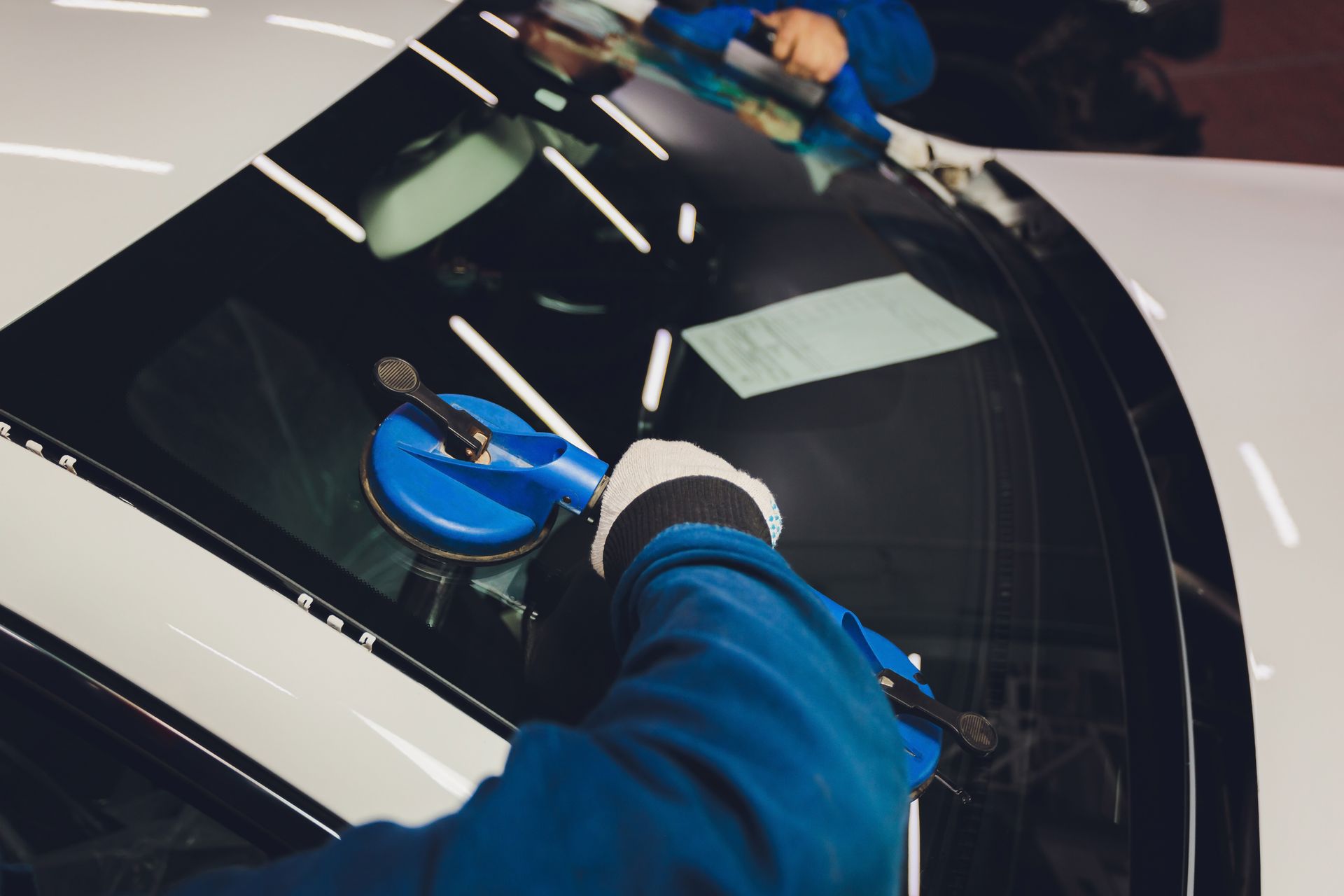 Person applying blue film to a car windshield with a squeegee