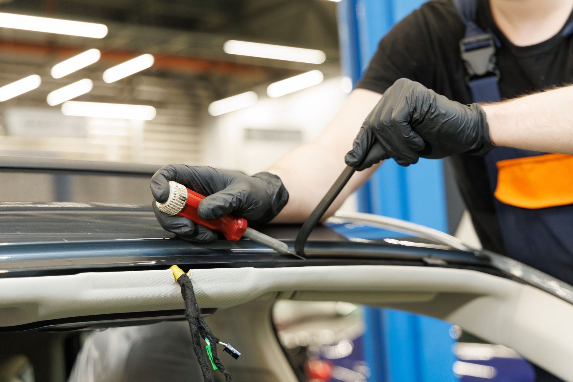 Mechanic using tools to repair a car windshield seal in a workshop