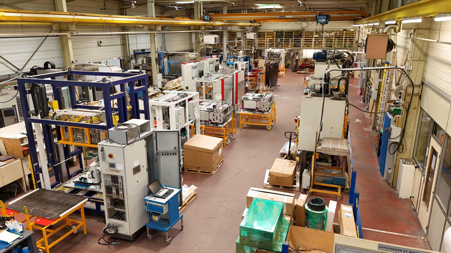 Vue aérienne d'une usine avec machines et caisses. Le décor est un intérieur industriel, centré sur la production.