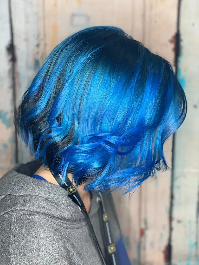 Side-profile of a person with bright blue wavy hair against a wood-paneled background