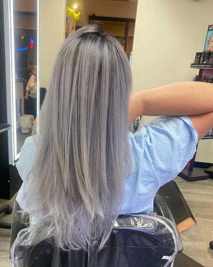 Person with long silver hair sitting in a salon chair, viewed from behind.