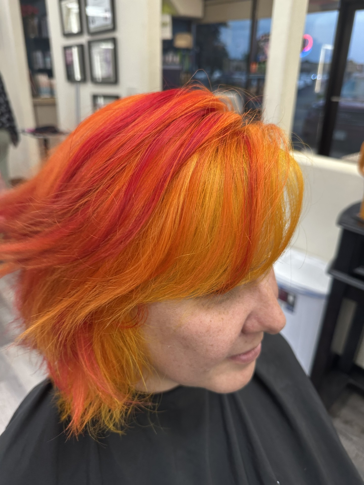 Person with bright orange and yellow layered hair in a salon chair, shown in profile.
