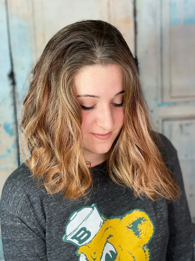 Woman with shoulder-length wavy hair looking down in a dark sweatshirt with a green and yellow graphic.