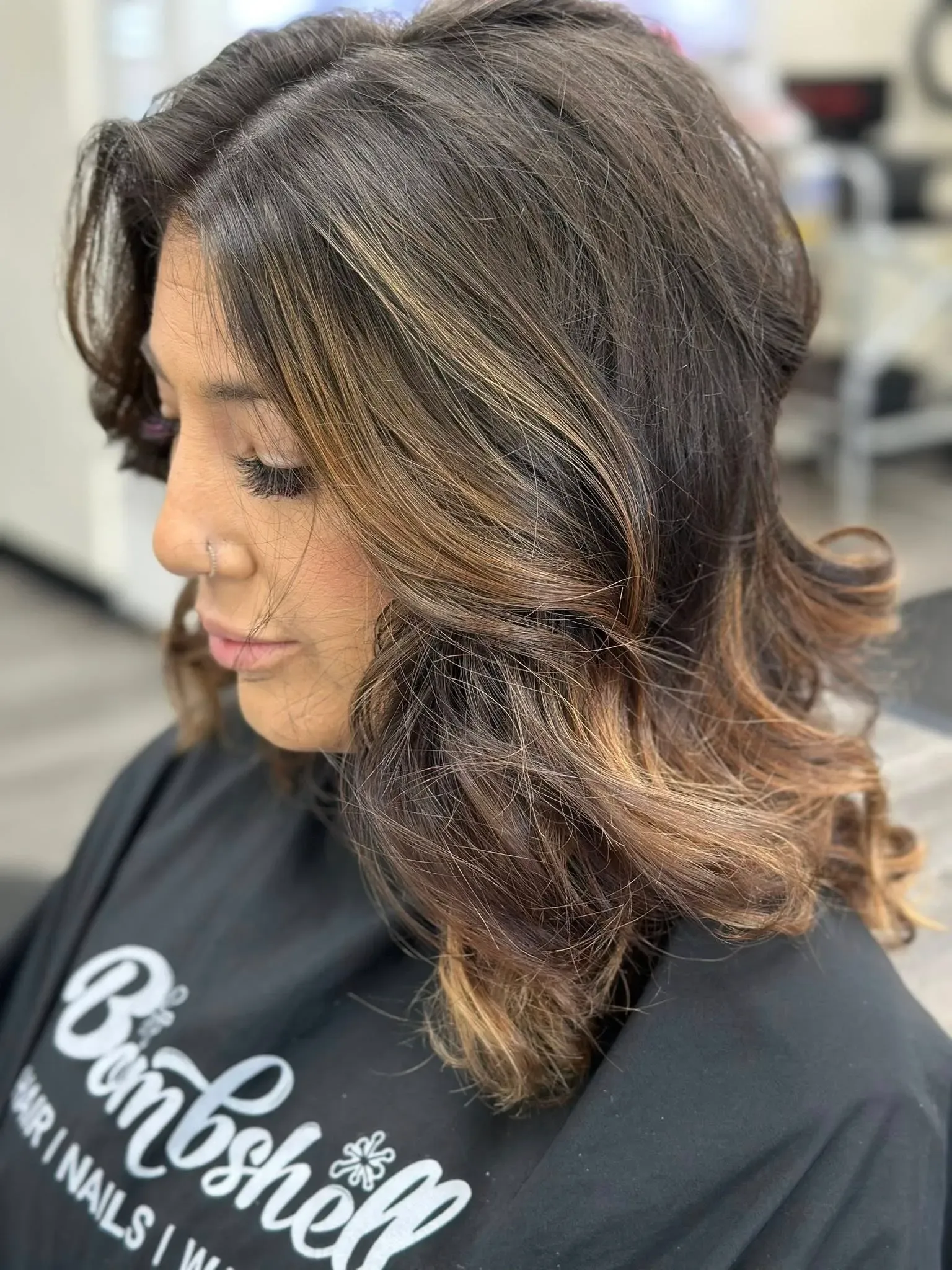 Side view of a woman with layered brunette hair and blonde highlights in a salon chair