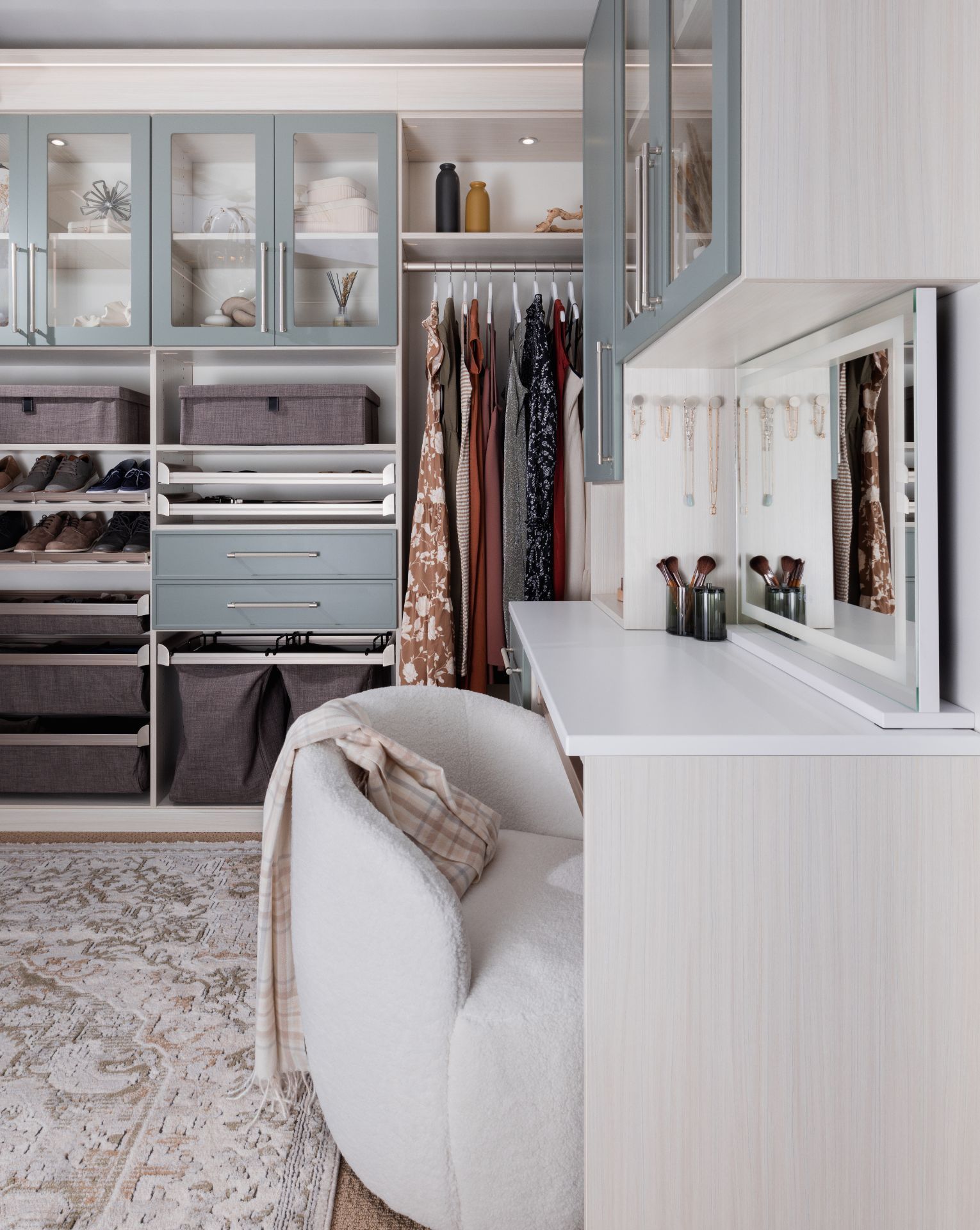 Walk-in closet with white shelving, hanging clothes, drawers, and a vanity bench by a mirrored counter.