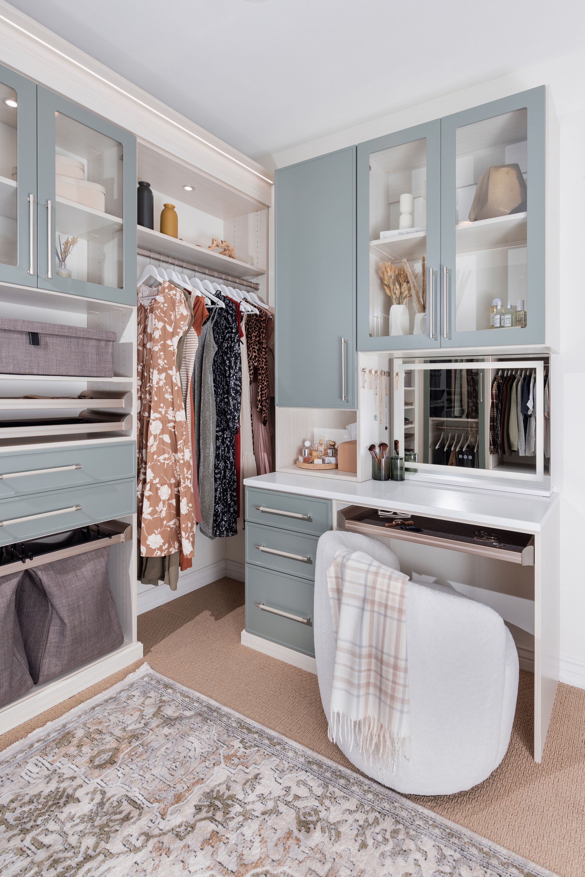 Bright walk-in closet with gray cabinets, hanging clothes, vanity desk, mirror, and chair