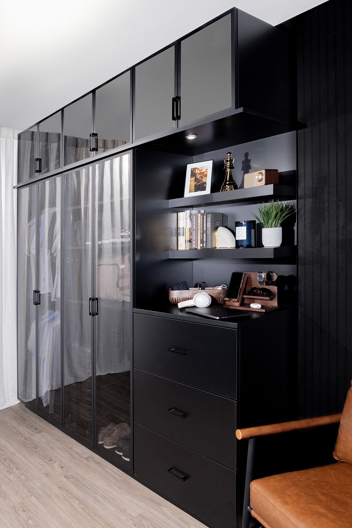 Modern black wardrobe with glass doors, shelves, and drawers in a light wood-floored room