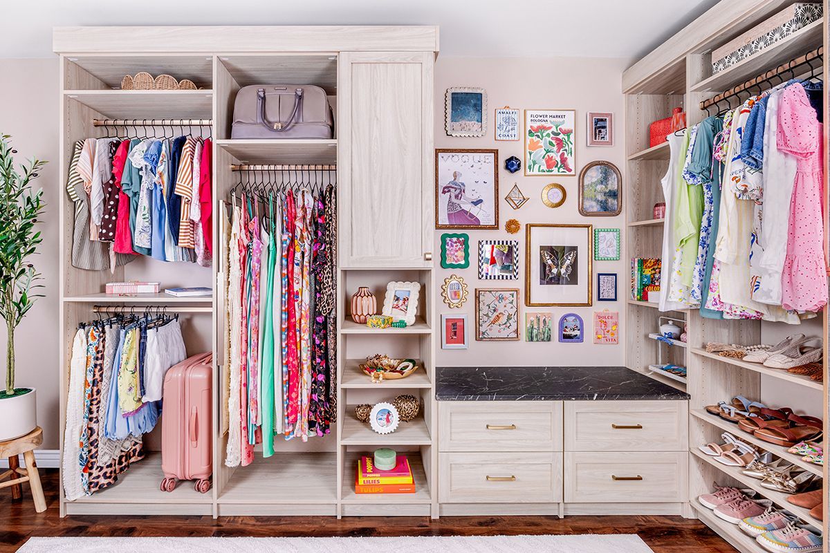Walk-in closet with white shelving, colorful clothes, drawers, and framed wall art