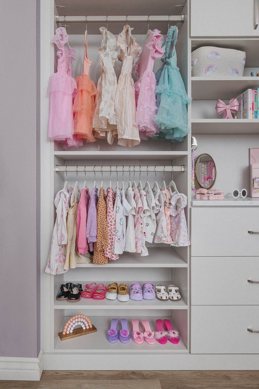 Children’s clothing and shoes neatly arranged in a closet with pastel dresses and toys.