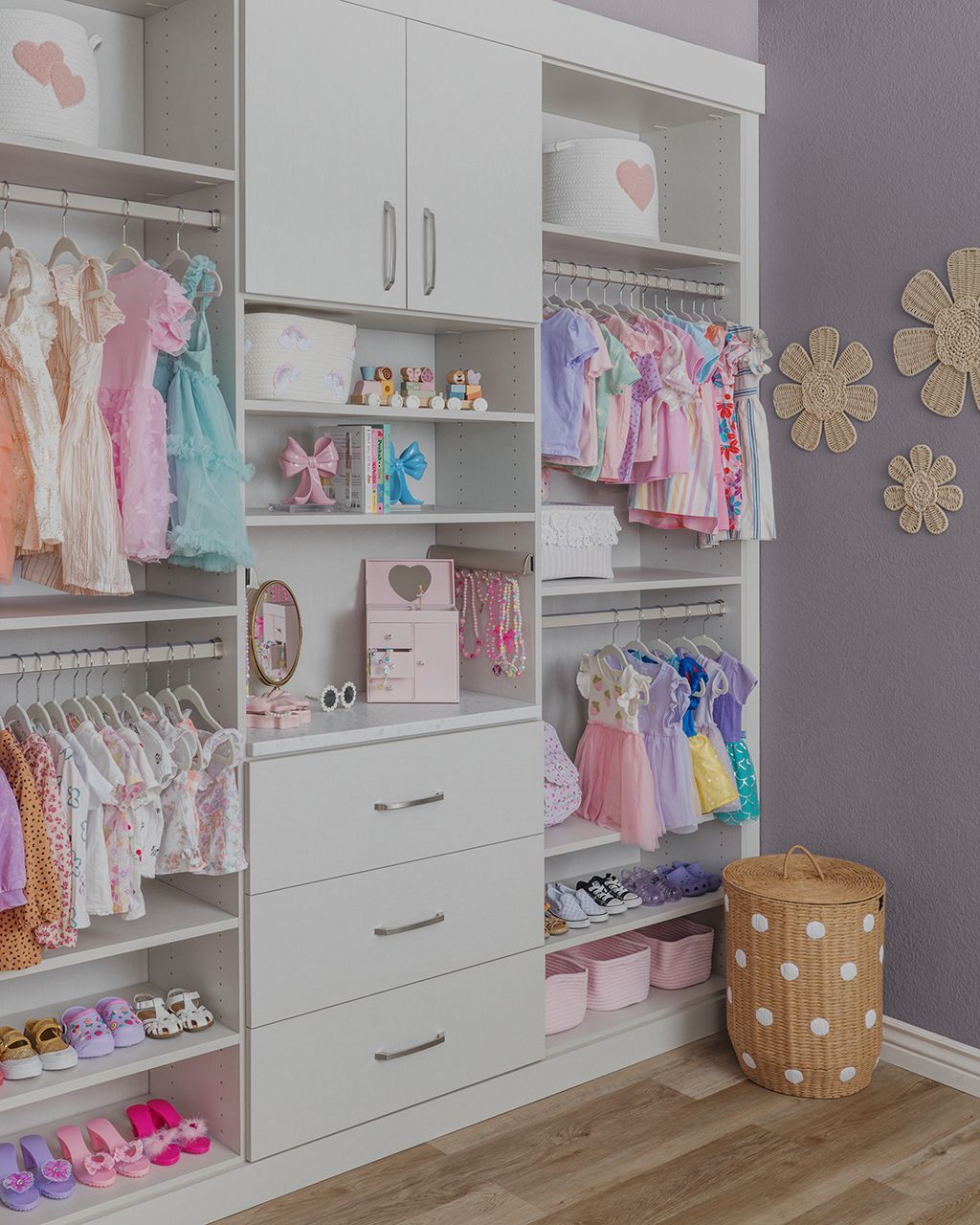 Pink-and-white children’s closet with hanging clothes, drawers, shelves, and woven basket against a gray wall