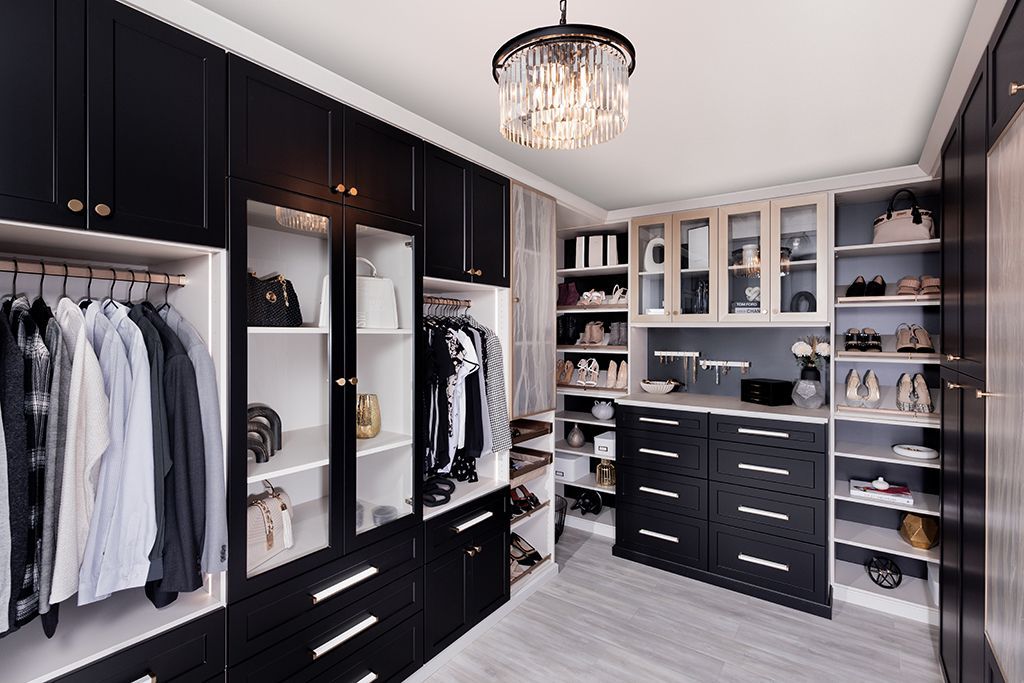 Elegant black-and-white walk-in closet with clothes, drawers, shelves, and a chandelier