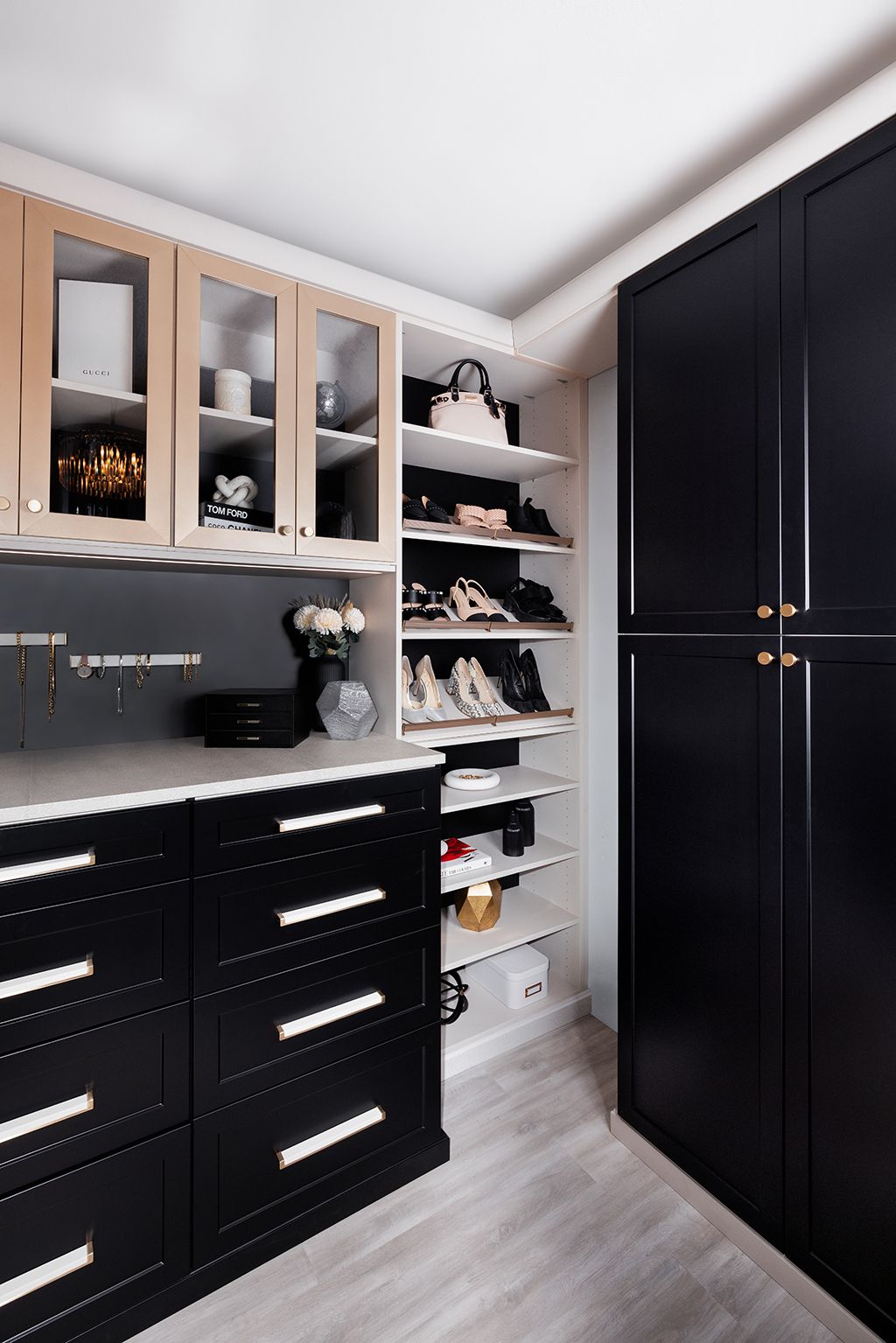 Walk-in closet with black drawers, open shoe shelves, and glass-front cabinets under slanted ceiling.