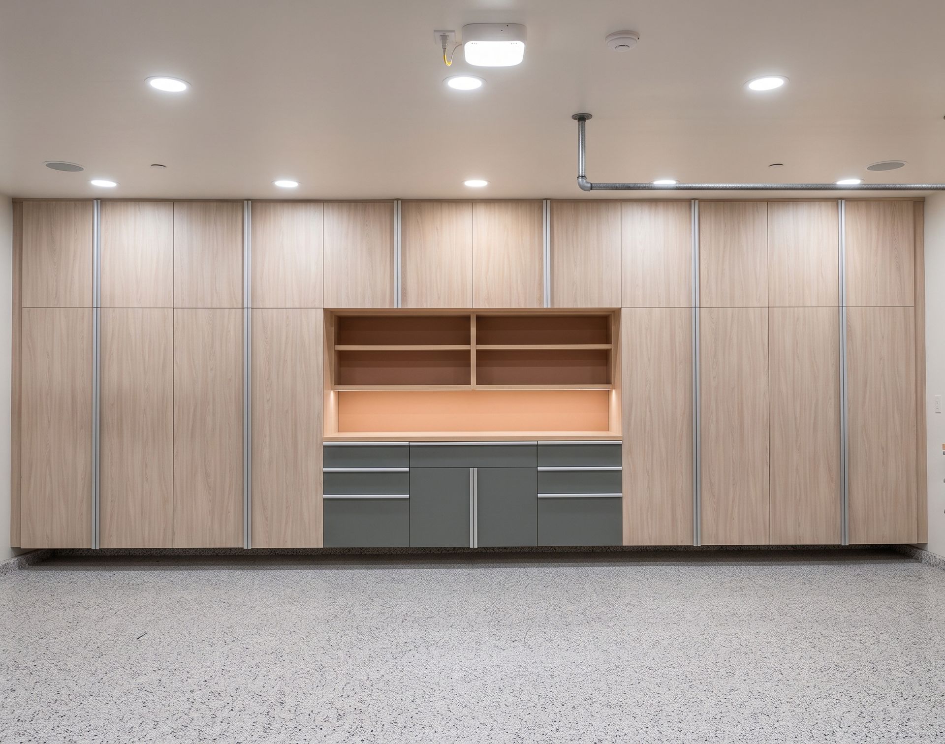 Built-in wood storage wall with gray cabinets under recessed ceiling lights in a room