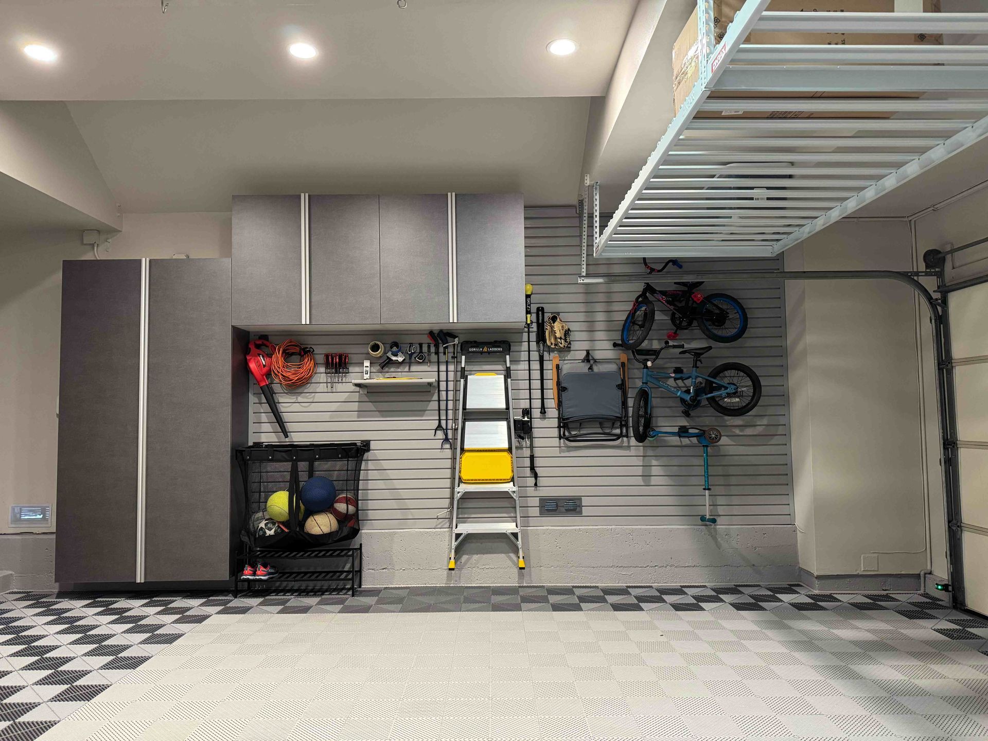 Garage with wall-mounted storage cabinets, hanging bikes, and a checkered floor under bright ceiling lights