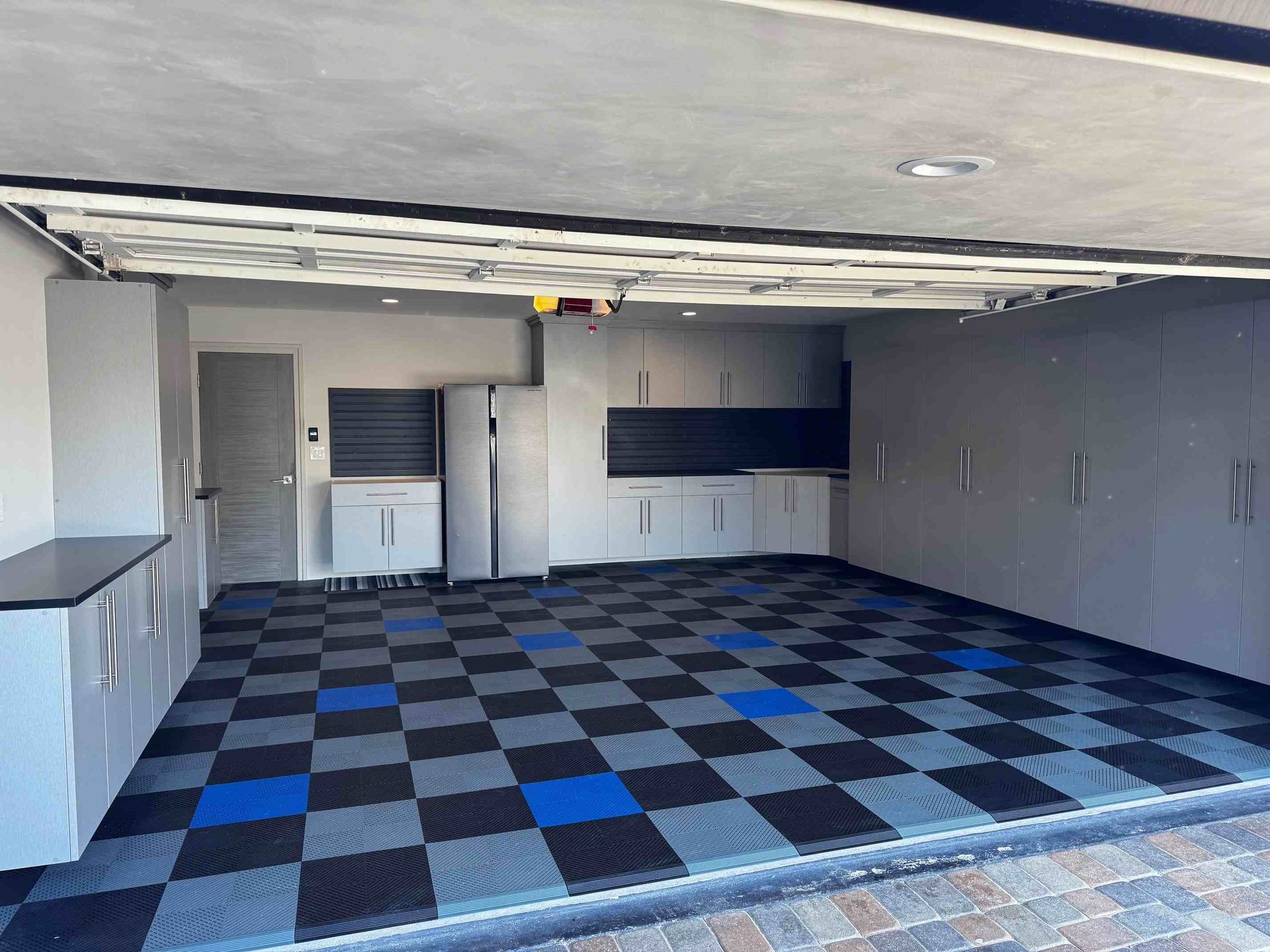 Empty garage with blue-and-black checkered floor, gray walls, and cabinets at the back.