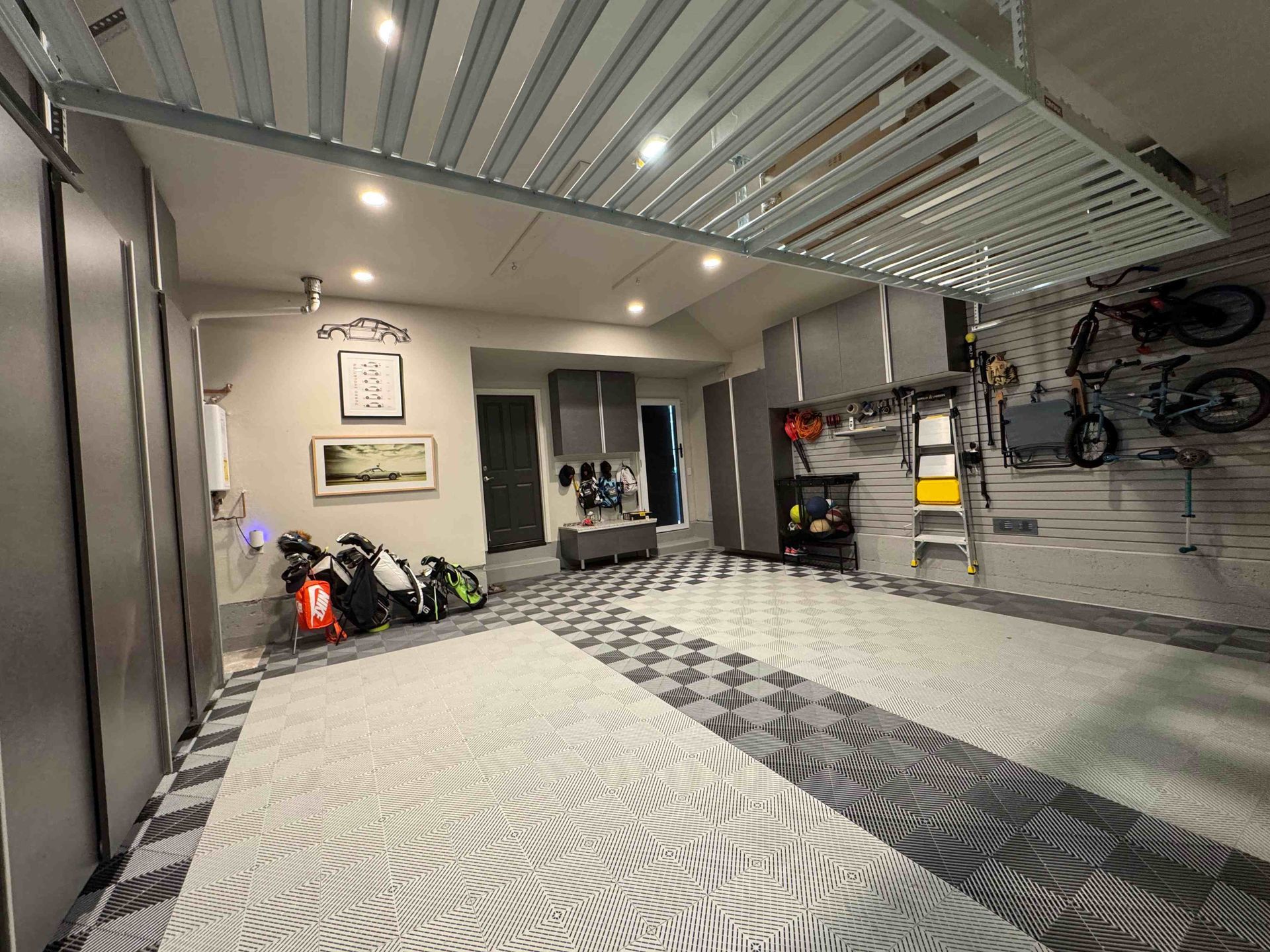 Modern garage interior with patterned floor, ceiling lights, wall storage, bikes, and sports gear.