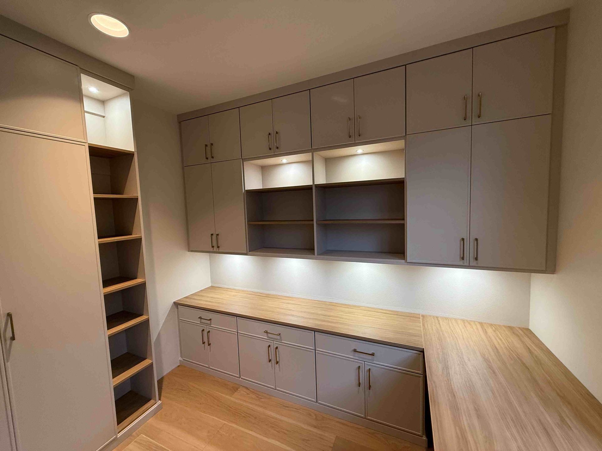 Empty walk-in closet with gray cabinets, wood countertops, and built-in shelving under warm lighting