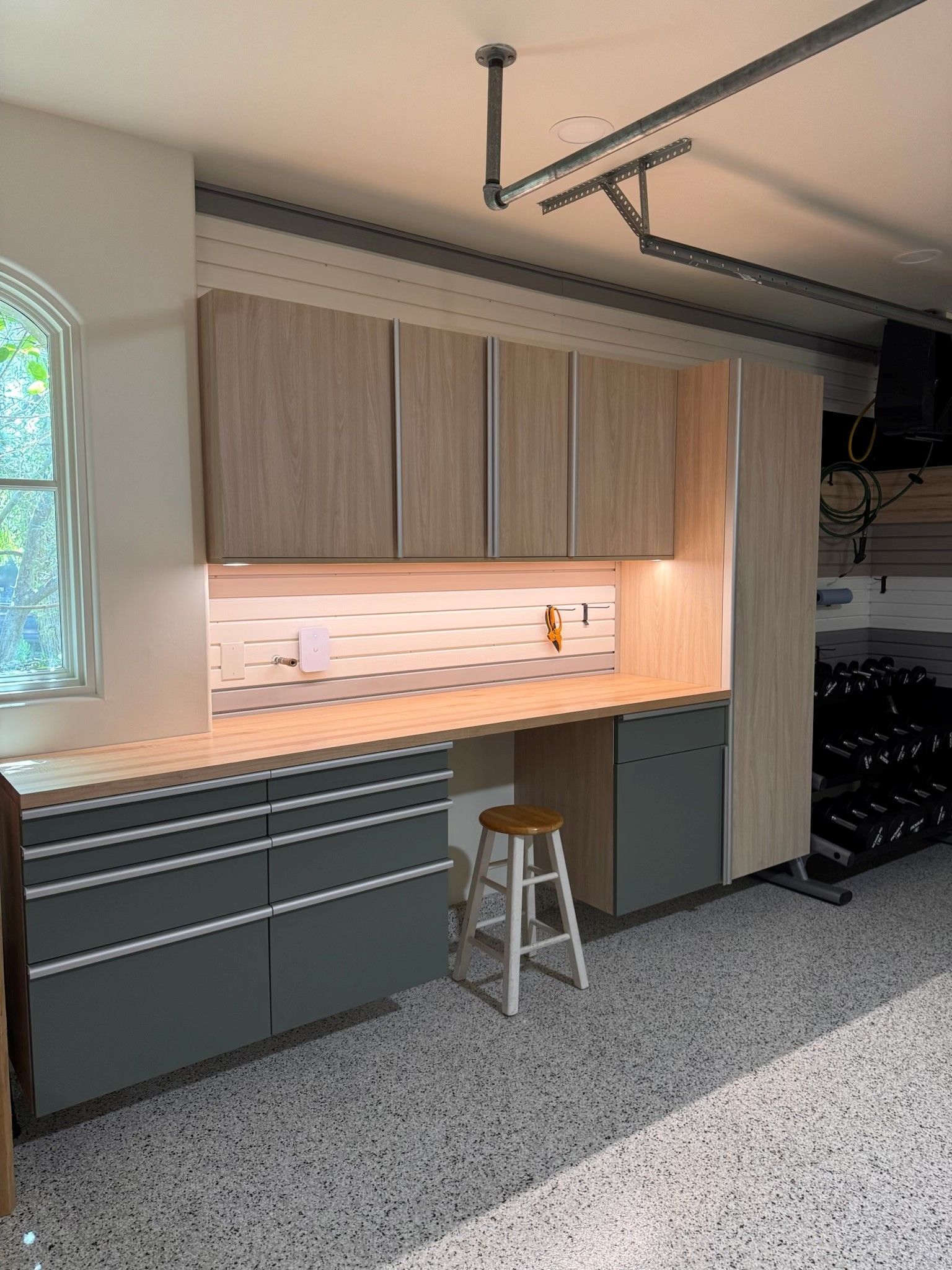 Modern garage workshop with wood cabinets, lighted backsplash, gray drawers, and a rolling stool