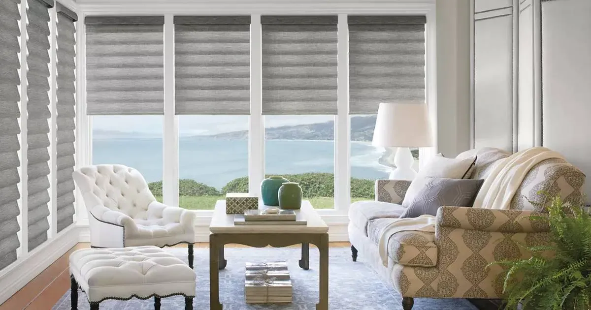 A living room with roman shades, a couch , chair , coffee table and sliding glass doors.