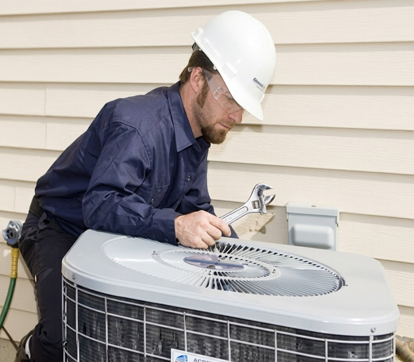 Technician in hard hat inspecting an outdoor air conditioning unit beside a house