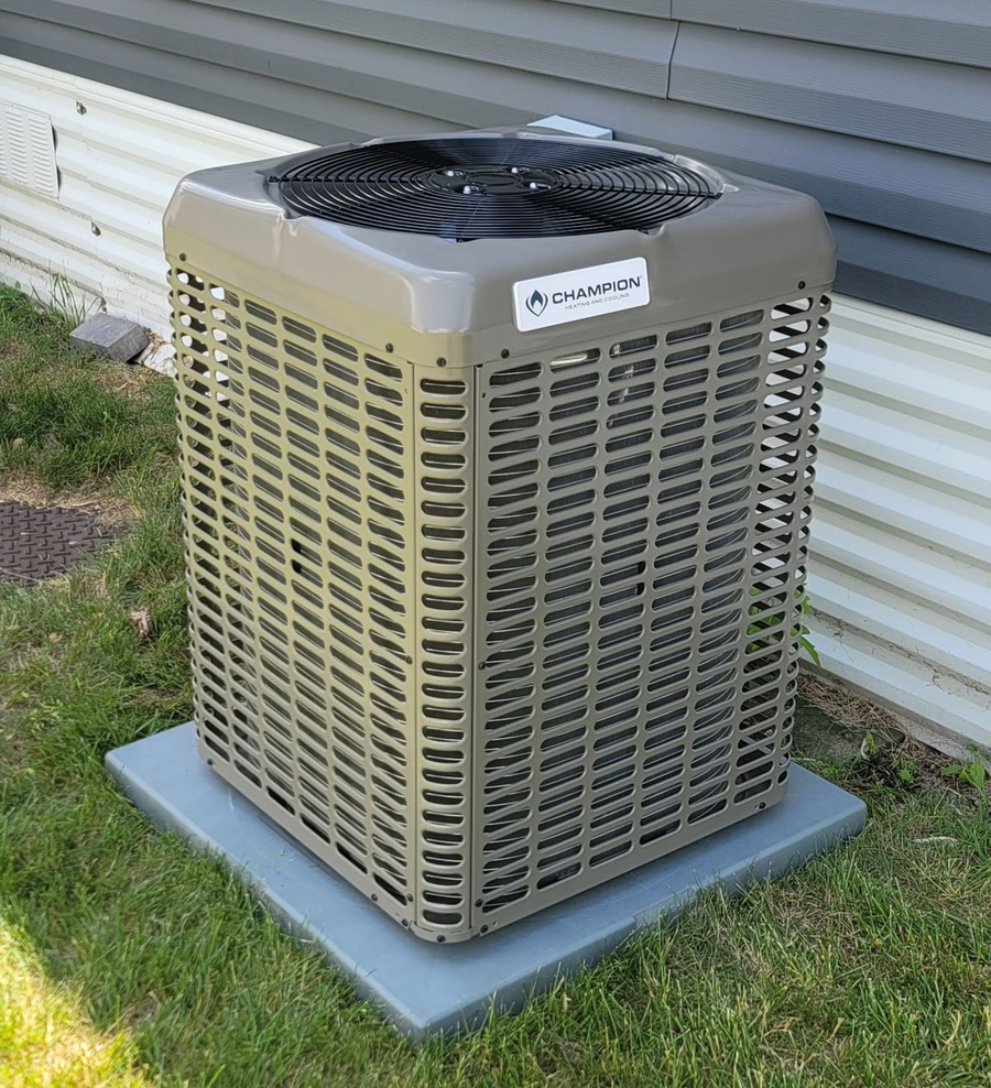 Outdoor HVAC air conditioning unit beside a house, with a tan grille and black fan on a concrete pad.
