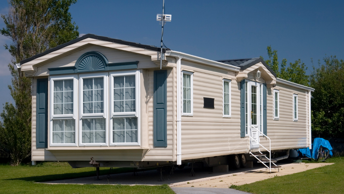 Beige mobile home with white trim and blue accents parked on a sunny lot