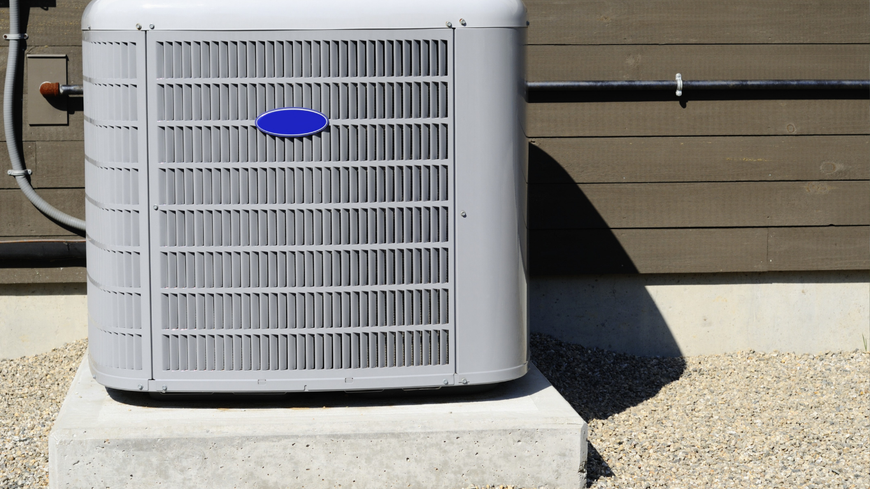 Outdoor air conditioning unit beside a house wall on a concrete pad and gravel
