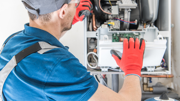 Technician in blue shirt and red gloves servicing an open wall-mounted boiler or HVAC unit
