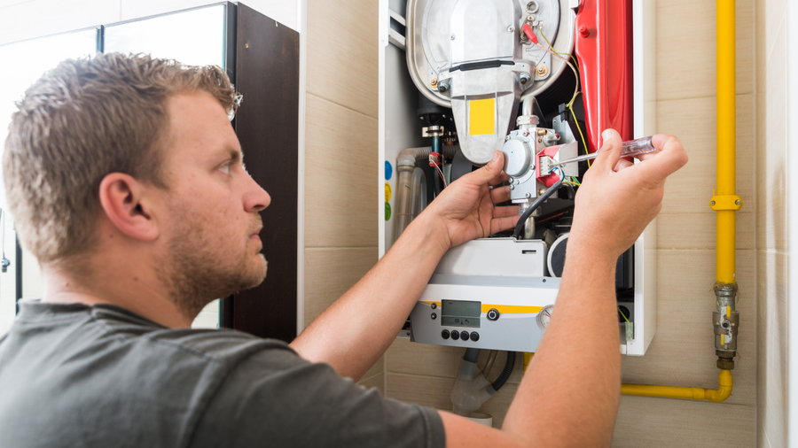 Technician inspecting a wall-mounted boiler with tools in a utility room