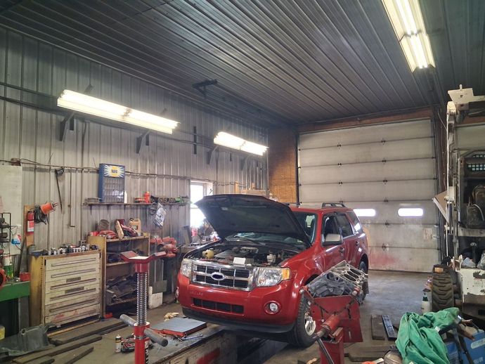 Red SUV with open hood in auto repair shop garage, surrounded by tools and equipment | Kensinger Repair Center
