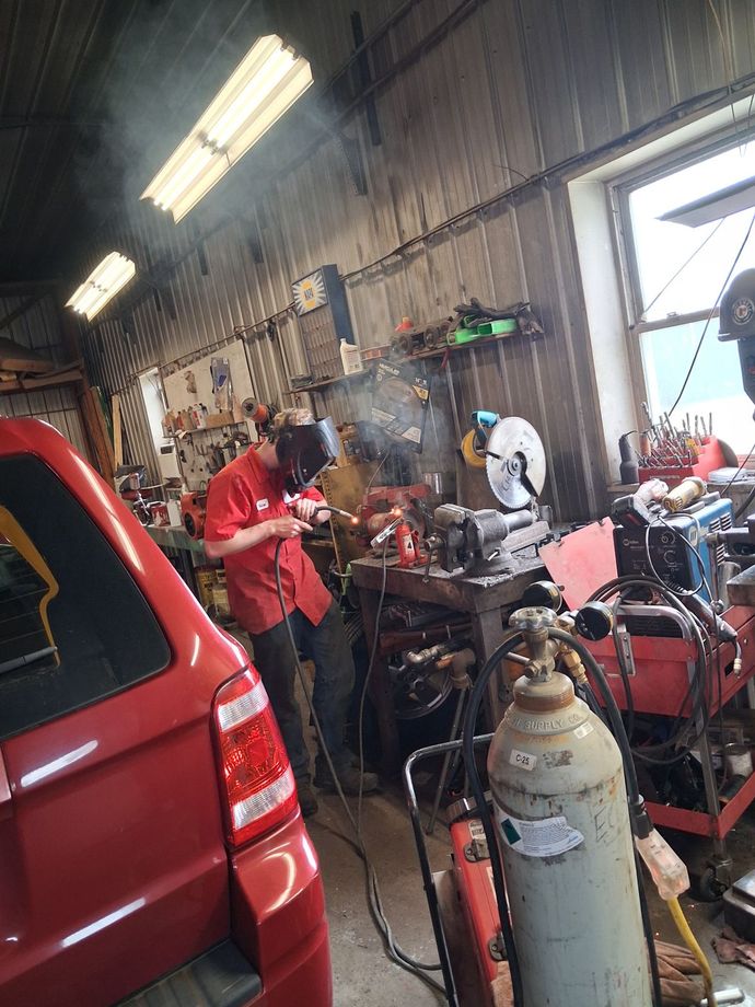 Red car with open hood in an auto repair garage, surrounded by tools and equipment. | Kensinger Repair Center