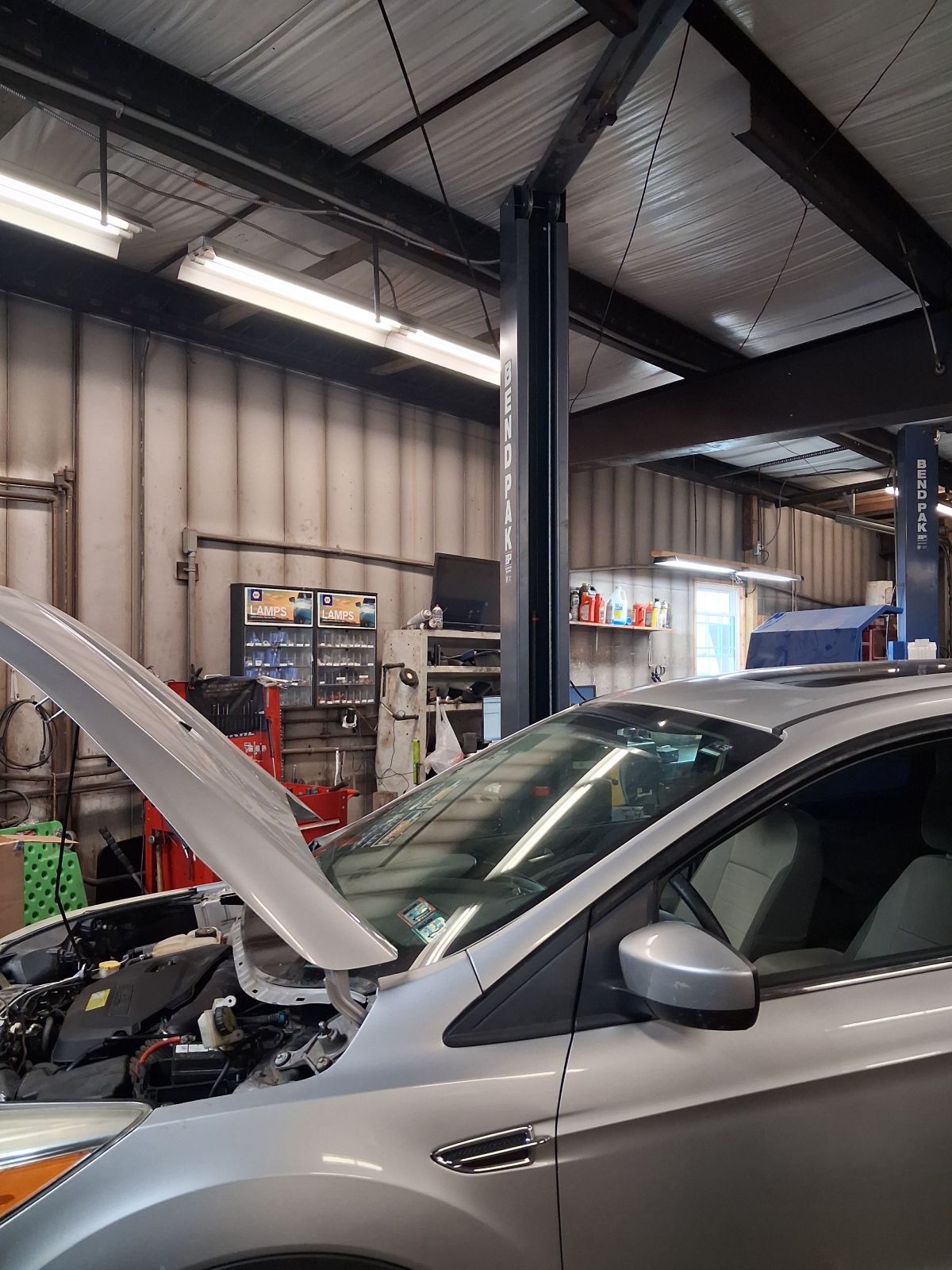 Silver car in an auto shop with hood open under industrial ceiling lights | Kensinger Repair Center