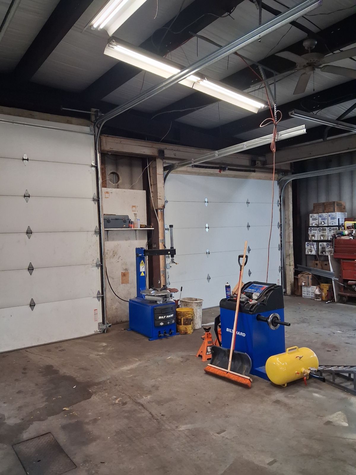 Industrial garage with two white roll-up doors, blue equipment, and a yellow tank on a concrete floor | Kensinger Repair Center