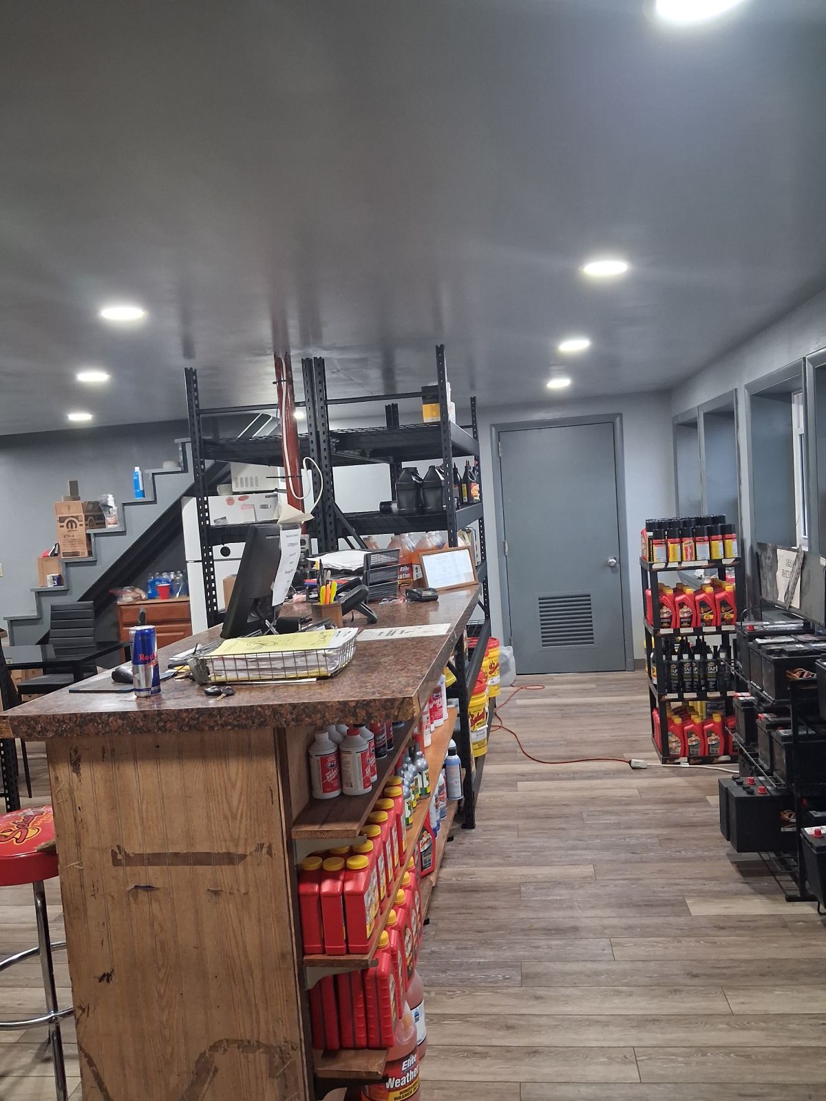 Small convenience store aisle with wooden counters, shelves of snacks, stairs, and bright ceiling lights. | Kensinger Repair Center